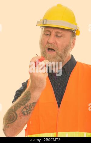 Close up of mature bearded man construction worker with hand tattoos eating apple Stock Photo