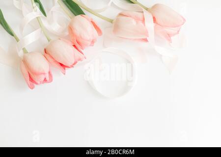 Hello spring. Pink tulips with ribbon and hearts on white background, flat lay. Stylish soft spring image. Happy womens day. Greeting card mockup with Stock Photo