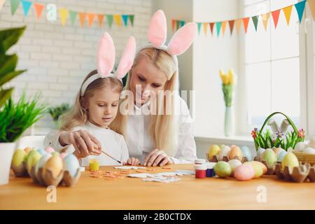 Happy easter. Daughter and mother with rabbit ears decorate Easter eggs sitting at a table Stock Photo