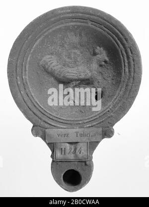 A gray-gray lamp with a round body on a recessed pedestal. The hollow mirror is surrounded by recessed concentric circles and is decorated with a relief of a rooster. The short, broad spout with a small fire hole is decorated with volutes. The small filling hole is to the right of the figure., Oil lamp, pottery, terracotta, 2.6 x 10.6 x 7.7 cm, 1st and 2nd century AD. 1-200, Africa Stock Photo