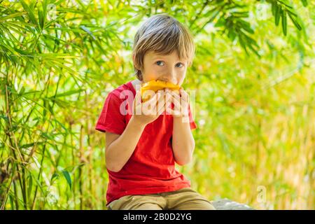 Little cute boy eating mango on the terrace Stock Photo