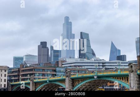 Iconic CIty of London skyscrapers and skyline of the financial district viewed over Southwark Bridge in cloudy wet weather in winter Stock Photo