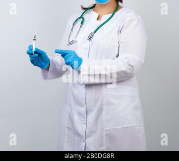 medic woman in white coat and blue latex gloves holds a syringe and points to it with his hand, white studio background