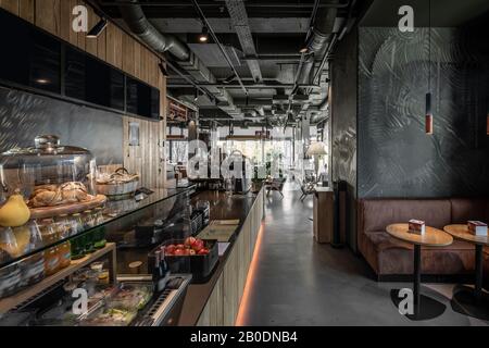 Cafe in a loft style with wooden walls and a gray floor. There is a wooden rack with glass showcase with food and fruit and desserts, tables with sofa Stock Photo