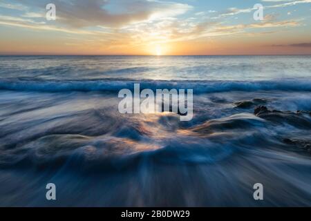 Water flows over rocks at sunset on the beach Stock Photo