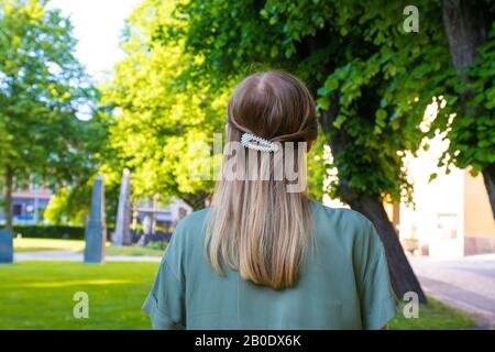 Back view young girl with blond hair and beautiful pearls hairpin and olive color dress in the park. Spring sunny day Stock Photo