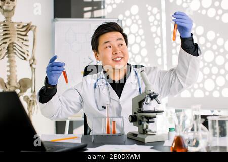 Asian Chinese doctor virologist scientist working in lab making medical research, using microscope, test tubes, equipment. Biotechnology, chemistry Stock Photo