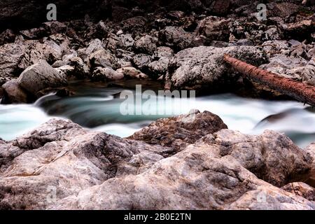 View to scenic mountain river with rapid and noisy stream of turquoise-blue water, rocks and a tree trunk across the river in natural park in Austria. Stock Photo