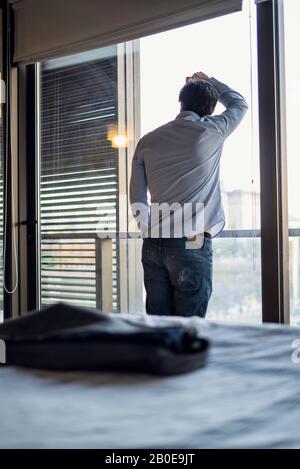 Thoughtful young man standing by the window Stock Photo