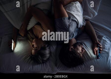 Young couple using smartphones on bed Stock Photo