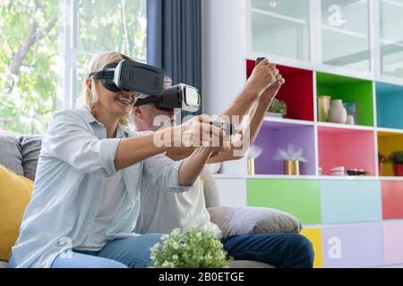 Two joyful seniors playing video games seated on a sofa at home. Stock Photo