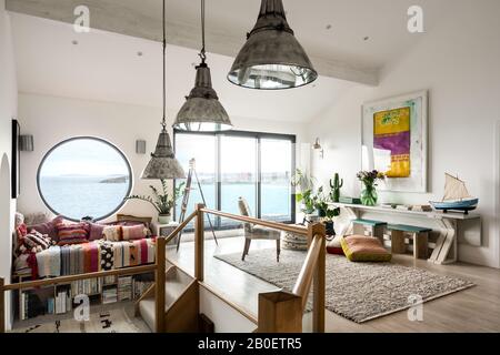 Reclaimed lights and large porthole window in split level 1960s renovation with view to Fistral Beach Stock Photo