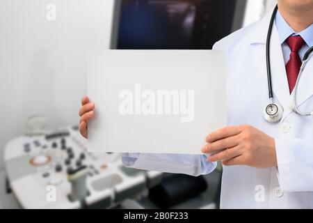 A male doctor holding a message board in front of an ultrasound diagnostic device Stock Photo