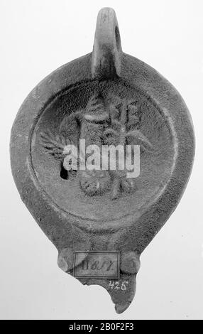 A red-nested lamp with an oval body on a recessed, round base. The concave mirror is surrounded by a recessed circle and decorated with a relief of a palm branch, a cornucopia and a Hermes staff. The short, broad spout was decorated with volutes. The vertically attached ear is decorated with notches. The small filling hole is to the left of the image. Brand: L.M.C. (?), oil lamp, earthenware, terracotta, 4.8 x 12.5 x 7.9 cm, 1st and 2nd century AD. 1-200 AD, Tunisia Stock Photo