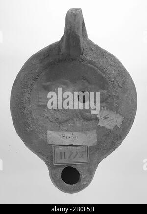 A brown-tinted light with a round body on a round base. The hollow, round mirror is surrounded with a recessed circle and decorated with a relief of a bird sitting on a branch. The small filling hole is in the figure. The short, blunt spout is round and has a large fire hole. The vertically attached ear is decorated with notches. The start of the spout is horizontal., Oil lamp, earthenware, terracotta, 3.7 x 10 x 7 cm, 2nd half 1st century to 1st half 3rd century AD. 50-250 AD, Tunisia Stock Photo