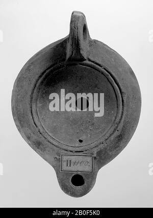 A brown-tinted light with a round body on a round base. The hollow, round mirror is surrounded with concentric circles and undecorated. The small filling hole is in the middle. The short, blunt spout is round and has a small fire hole. The vertically attached ear is decorated with notches. The spout of the spout is heart-shaped and deposited with three points. Brand: CCLO.SVC and X below, oil lamp, earthenware, terracotta, 5.1 x 10.9 x 7.8 cm, 2nd half 1st century to 1st half 3rd century AD. 50-250 AD, Tunisia Stock Photo