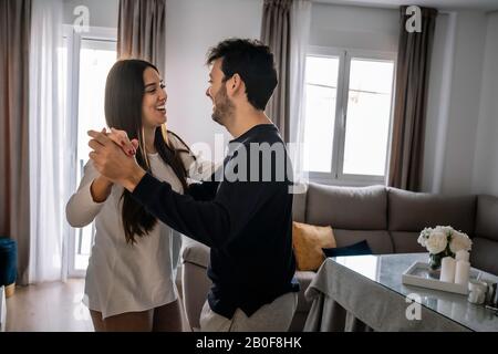 young couple smiling, dancing inside their house Stock Photo