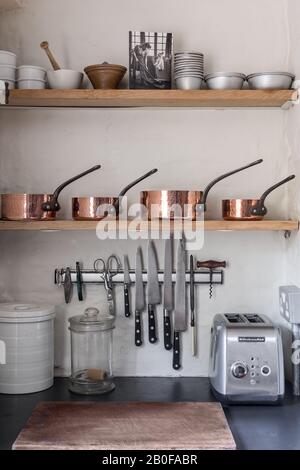 Antique copper pots with carbon steel Sabatier knives on a magnetic rack Stock Photo