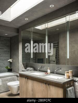 Large mirrored cabinets with double basins below skylight in modern West London apartment. Stock Photo