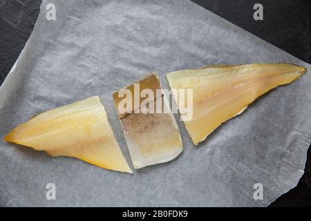 A smoked, undyed haddock fillet, Melanogrammus aeglefinus, bought from a supermarket fish counter in the UK and displayed on baking paper. It has been Stock Photo