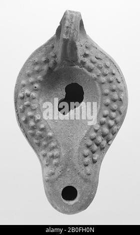 A brown-tinted light with a round body. The oval, concave mirror is surrounded by a slightly upright edge with the small filling hole in the middle. There are relief points on the shoulder. The short, broad spout is round closed and has a small fire hole. The vertically attached ear is decorated with notches. Brand: O, oil lamp, pottery, terracotta, 4.7 x 11.2 x 6.2 cm, 1st century AD. 1-100, Africa Stock Photo