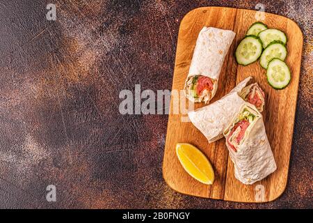 Wrapped sandwich with salmon, lettuce, cucumber and cream cheese, top view. Stock Photo