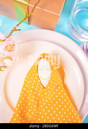 Beautiful festive Easter table setting with yellow napkin polka dot and smiling egg. Stock Photo
