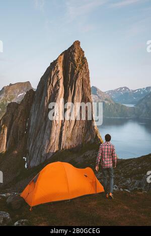 Camping tent and man solo traveler hiking in Norway sustainable travel adventure healthy lifestyle active summer vacations sunset Segla rock peak and Stock Photo