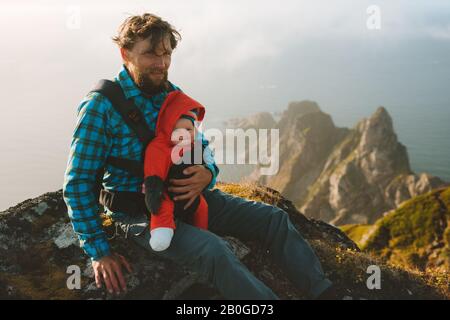 Father hiking with baby family traveling in Norway healthy lifestyle outdoor adventure summer vacations dad with child together on mountain top Stock Photo