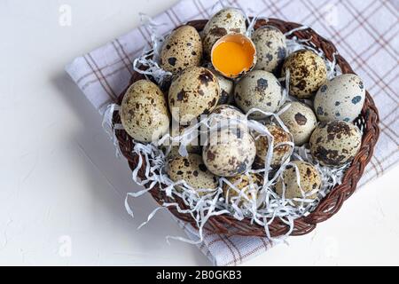 Quail eggs are placed in a wicker basket next to a willow twig. Getting ready for Easter. On white background. Copy space Stock Photo