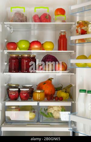 Variety glass jars homemade fruit and berry jams and fresh vegetables and fruits stand in fridge. Fermented healthy vegetarian food. Stock Photo