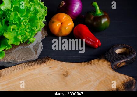 The cutting board is on the kitchen table next to a set of fresh vegetables for the summer salad Stock Photo