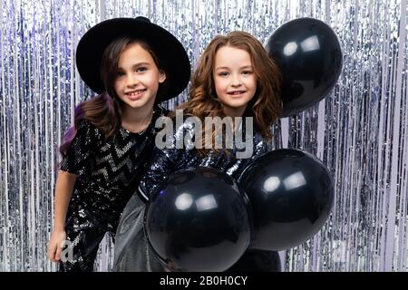 black Friday. two cute stylish young girls in holiday dresses with black balloons on a shiny background Stock Photo