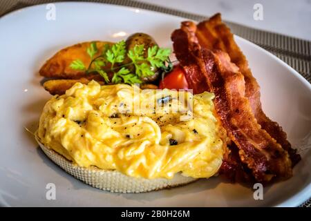 truffle egg with bacon strips and potato wedges on white plate Stock Photo