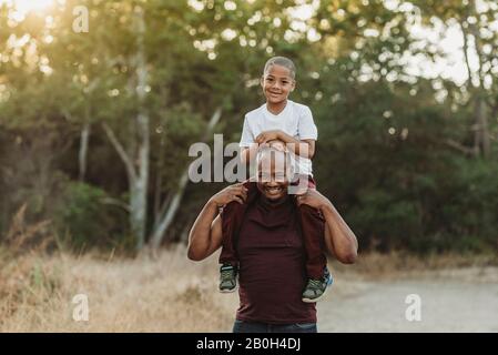Close up portrait of school-aged son sitting on father's shoulders Stock Photo