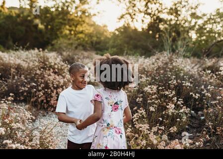 Close up view of brother and sister holding hands and playing in field Stock Photo