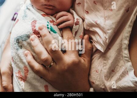 Macro overhead view of mother holding newborn boy's fingers in hospita