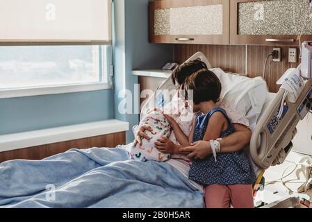 Wide view of mother holding newborn son meeting siblings Stock Photo