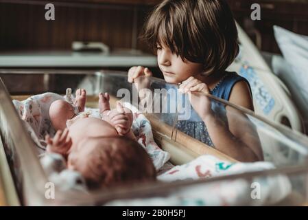 Sister looking at newborn brother in hospital bassinet Stock Photo