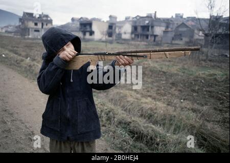 8th January 1994 Ethnic cleansing during the war in central Bosnia: a young boy poses with a home-made toy gun in Grbavica, on the outskirts of Vitez. In the background are burned houses and buildings, attacked by HVO (Bosnian Croat) forces four months before. Stock Photo