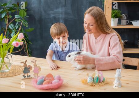 Smiling mother stroking fluffy rabbit together with excited son while celebrating Easter Stock Photo