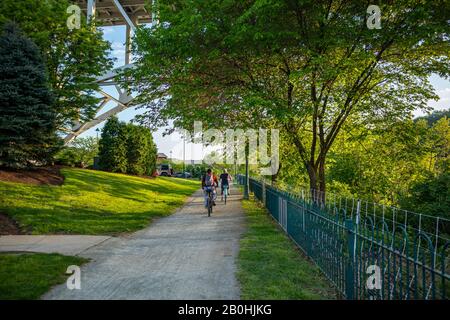 People riding bikes on a path, under green trees in spring. A place for relaxation and activities. Pittsburgh, Pennsylvania, USA. Stock Photo