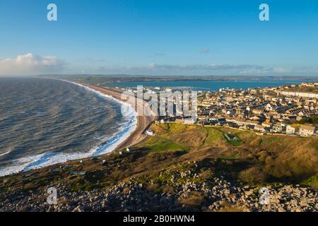 Fortuneswell, Portland, Dorset, UK.  20th February 2020.  UK Weather.  View from the top of the cliffs of West Weares across Fortuneswell on the Isle of Portland in Dorset during late afternoon sunshine with gusty winds and rough seas crashing ashore on Chesil Beach at Chiswell. Picture Credit: Graham Hunt/Alamy Live News Stock Photo