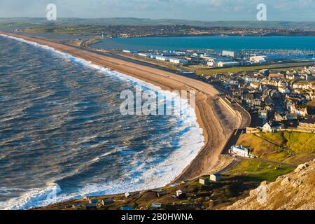 Fortuneswell, Portland, Dorset, UK.  20th February 2020.  UK Weather.  View from the top of the cliffs of West Weares across Fortuneswell on the Isle of Portland in Dorset during late afternoon sunshine with gusty winds and rough seas crashing ashore on Chesil Beach at Chiswell. Picture Credit: Graham Hunt/Alamy Live News Stock Photo