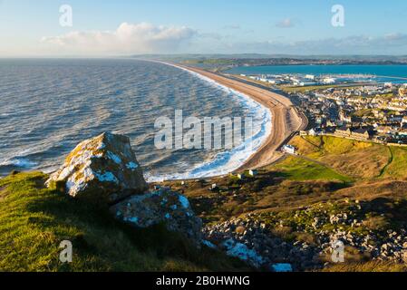 Fortuneswell, Portland, Dorset, UK.  20th February 2020.  UK Weather.  View from the top of the cliffs of West Weares across Fortuneswell on the Isle of Portland in Dorset during late afternoon sunshine with gusty winds and rough seas crashing ashore on Chesil Beach at Chiswell. Picture Credit: Graham Hunt/Alamy Live News Stock Photo