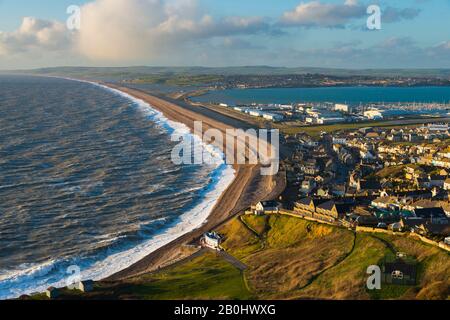 Fortuneswell, Portland, Dorset, UK.  20th February 2020.  UK Weather.  View from the top of the cliffs of West Weares across Fortuneswell on the Isle of Portland in Dorset during late afternoon sunshine with gusty winds and rough seas crashing ashore on Chesil Beach at Chiswell. Picture Credit: Graham Hunt/Alamy Live News Stock Photo