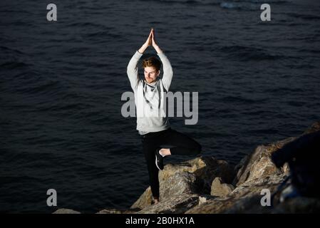Young redhead practicing yoga, Vriksasana tree posture, to concentrate and help him with his mindfullness Stock Photo