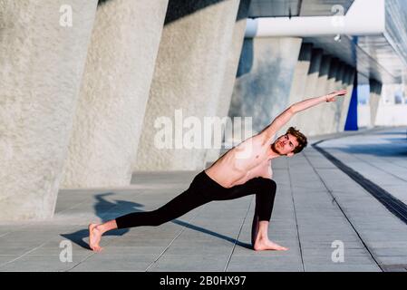 Young male athlete performing stretching exercises for back and arms in an urban place. Stock Photo