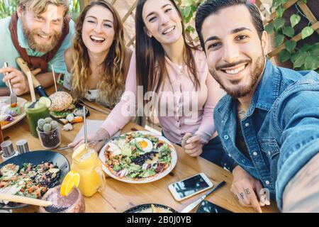 Happy friends taking selfie with mobile smartphone while lunching in coffee brunch restaurant - Young trendy people having fun eating together Stock Photo