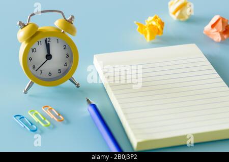 A yellow alarm clock next to swept balls of paper and a notebook. Place for text. Office concept